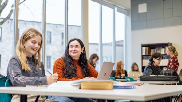 Photo de deux étudiantes assises à une table au Vie-Voir, local pour les élèves de Sciences humaines.