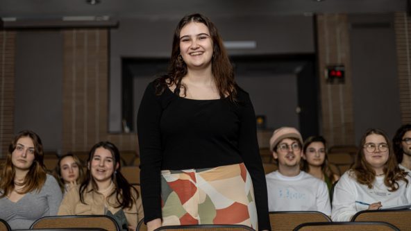 Photo d'une étudiante debout entouré d'élèves assis autour d'elle.
