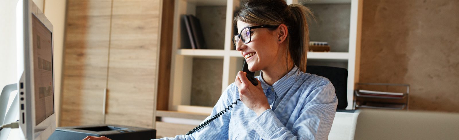 Femme souriante portant des lunettes qui parle au téléphone à un bureau.