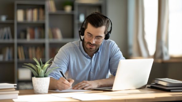 Homme avec casque d'écoute assis devant un portable.
